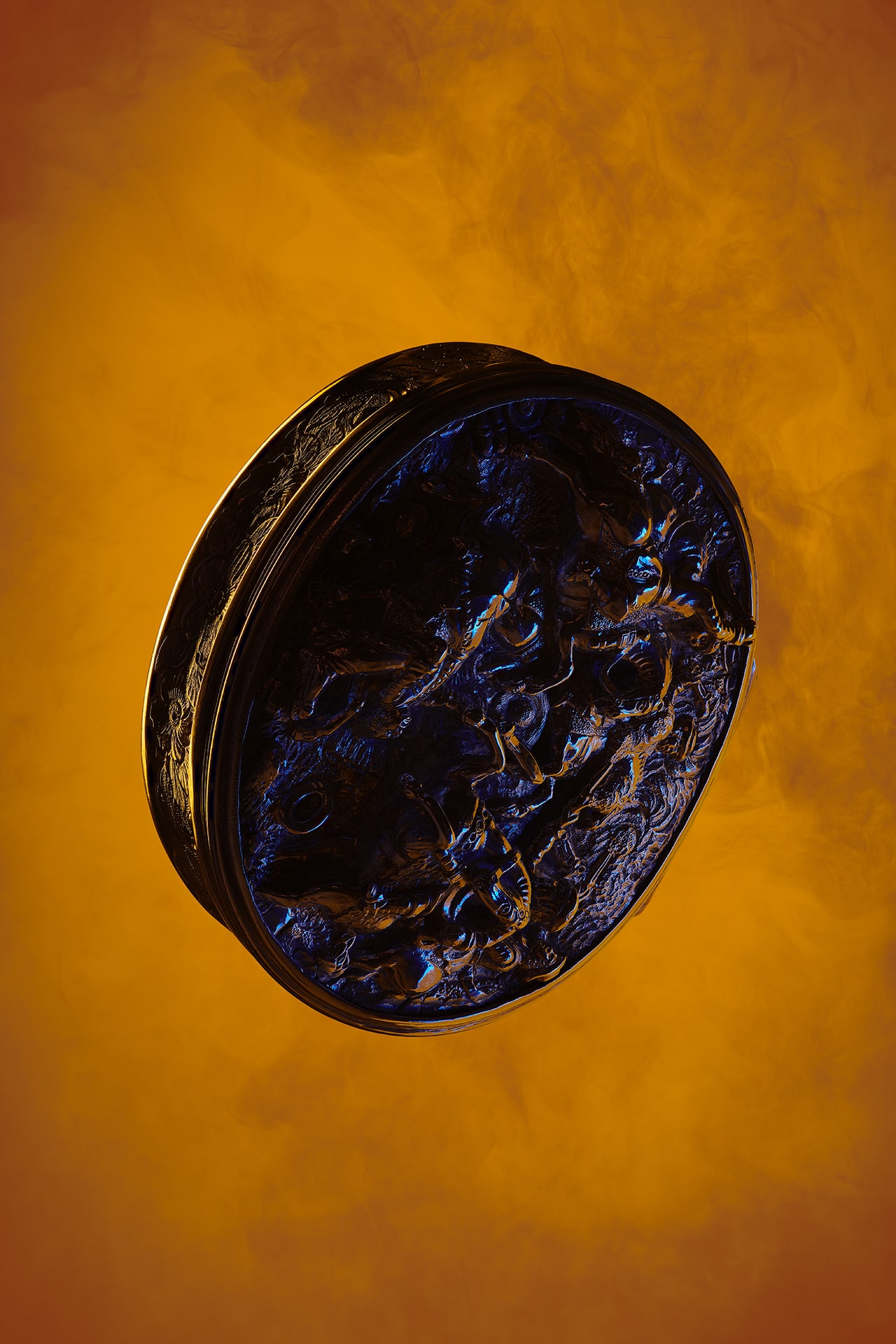 Circular dark object with raised pattern, on an orange smokey background