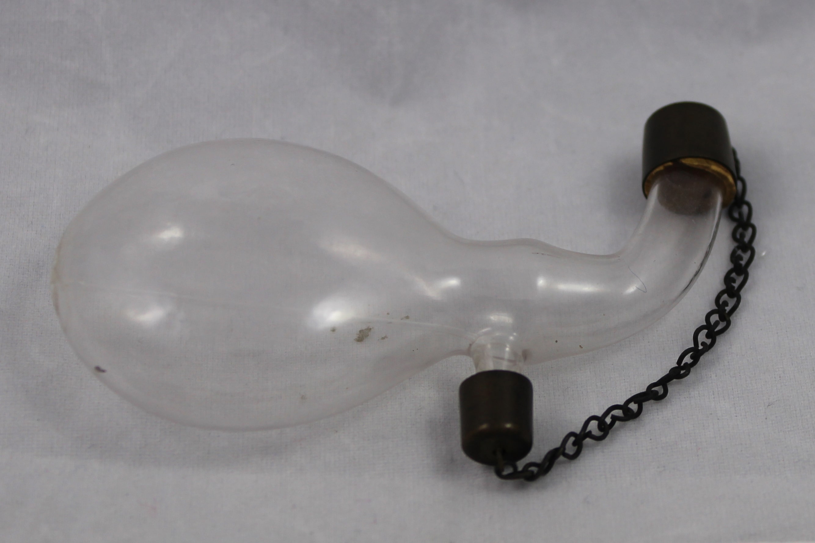 Circular glass flask with two necks, metal gap on each neck, caps connected by a small chain