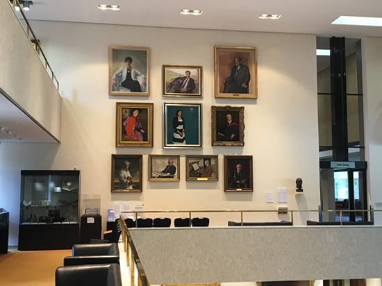 Photograph of a double-height wall hung with paintings of men and women.