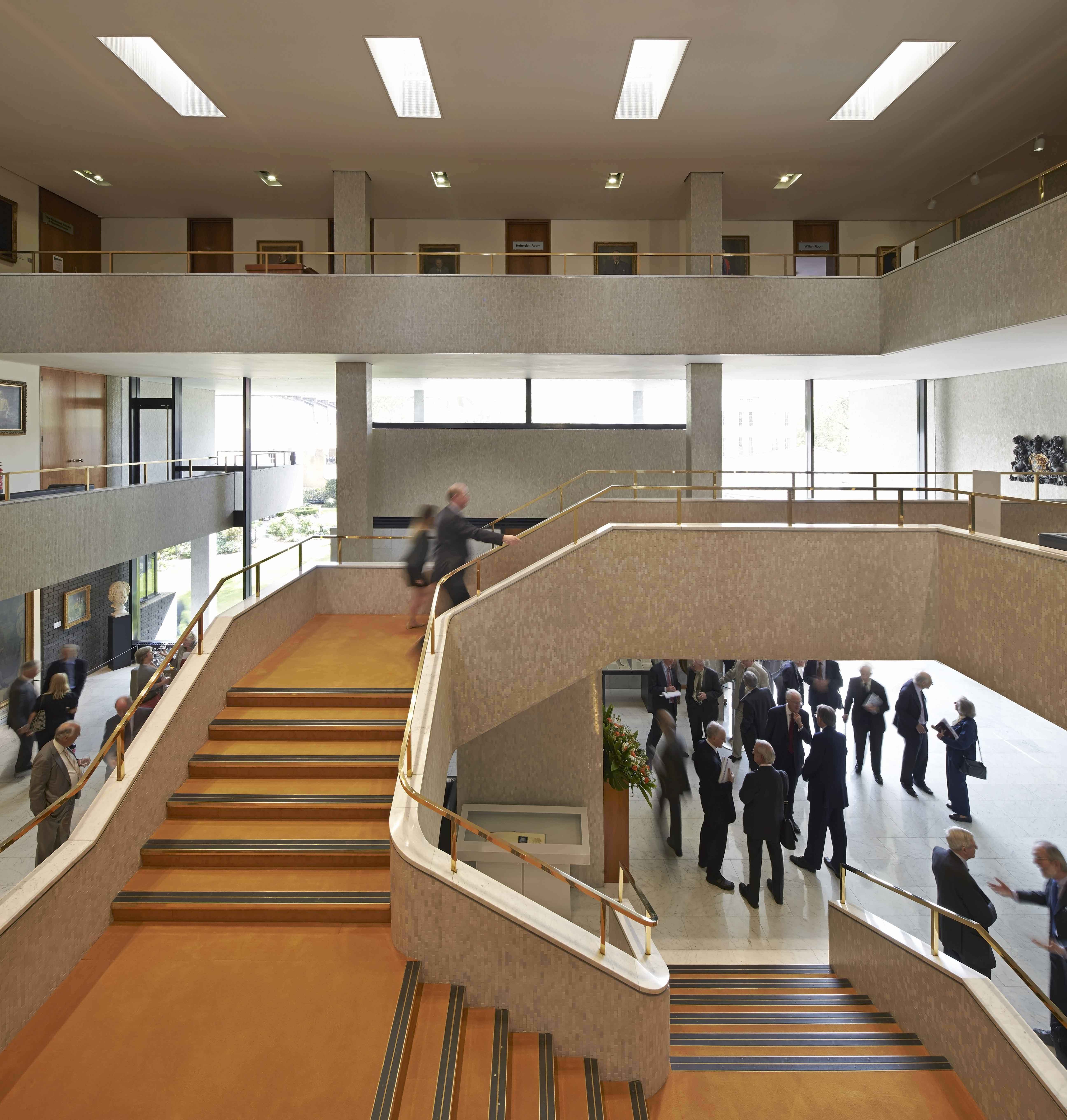 Interior of a building. A suspended staircase with orange carpet occupies most of the frame.