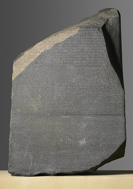 Photograph of a slab of dark stone inscribed with writing in three languages.