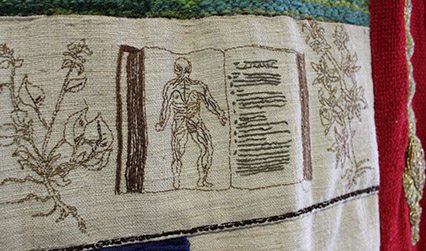 Photograph of an embroidered tapestry depicting pages from historical books about anatomy and medicinal plants.
