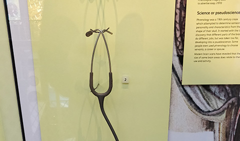 Photograph of a doctors' stethoscope with one earbud missing, mounted in a museum display.