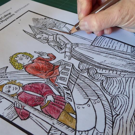 A white hand colouring in a picture using coloured pencils.